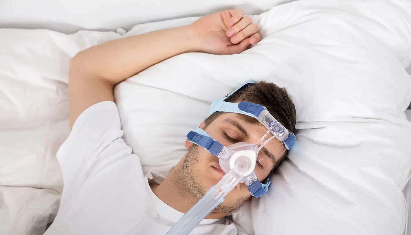 High-angle view of a man lying on bed using a clean CPAP machine to reduce the risk of getting a CPAP bacterial infection.